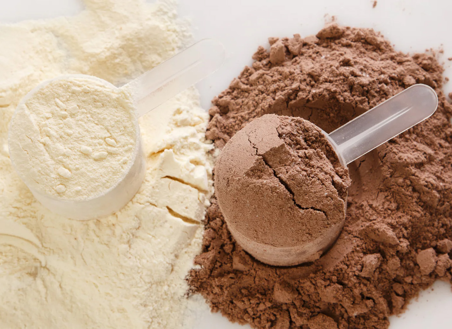 Two separate piles of protein powder with scoops: one of whey and one of plant protein