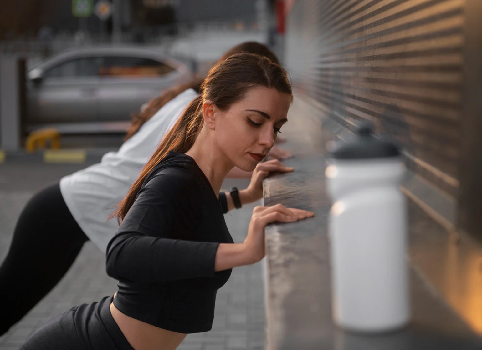 Two women stretching before exercising with a protein shaker