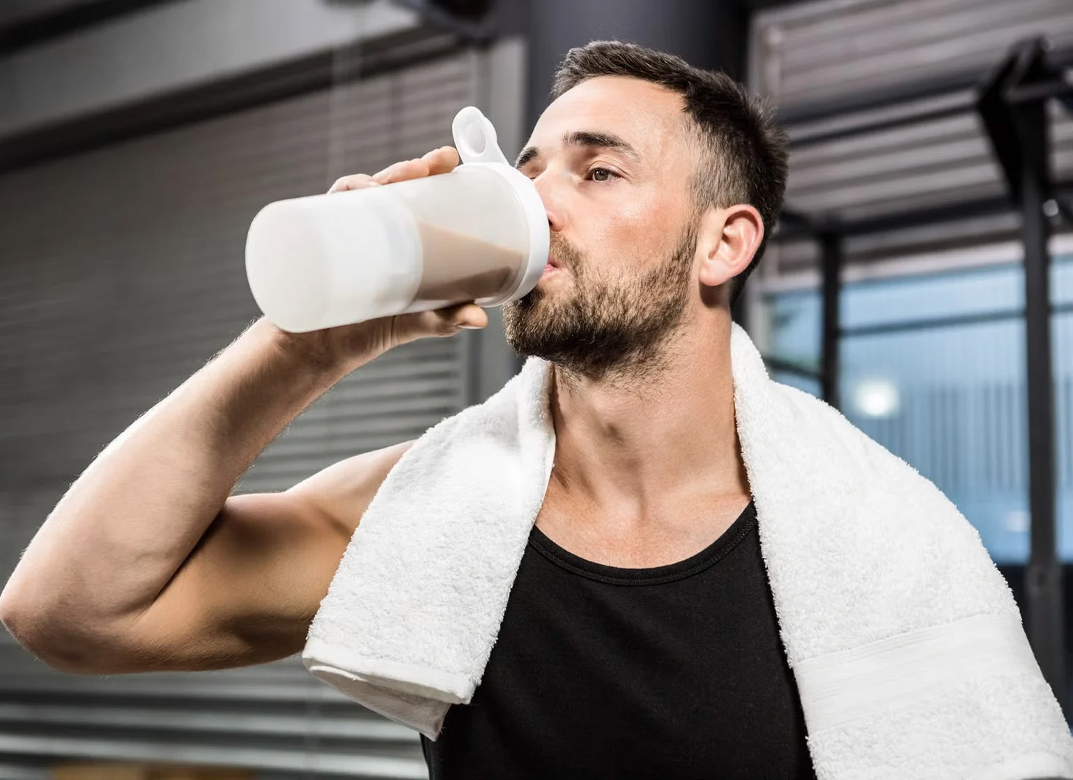 Man with a towel over his shoulders drinking a protein shake