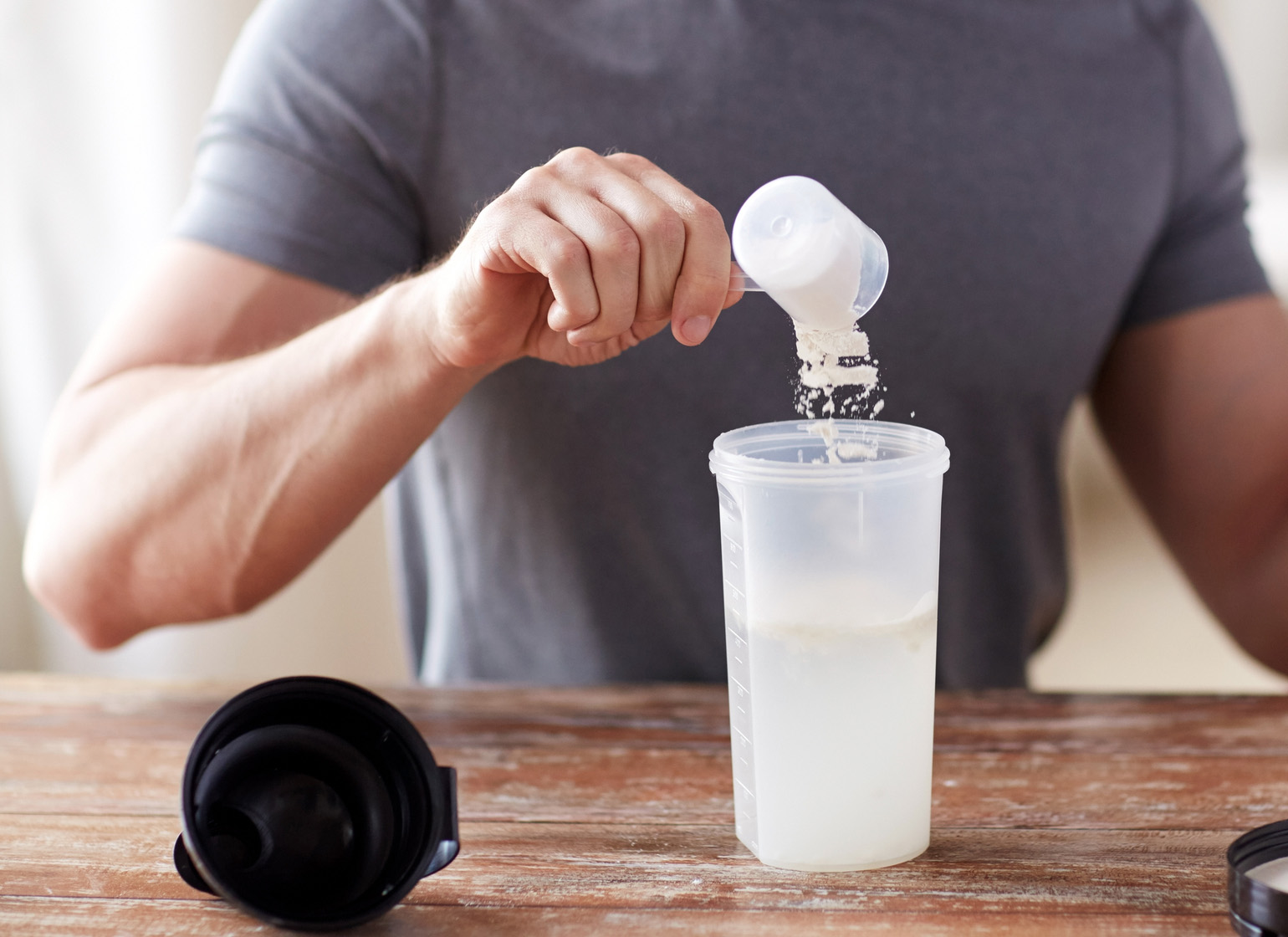 Man pouring a scoop of protein powder into shaker